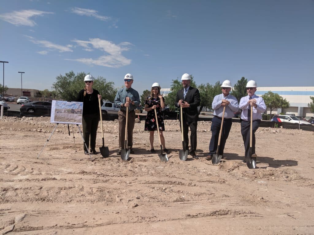 Groundbreaking ceremony with people holding shovels in a dirt field.