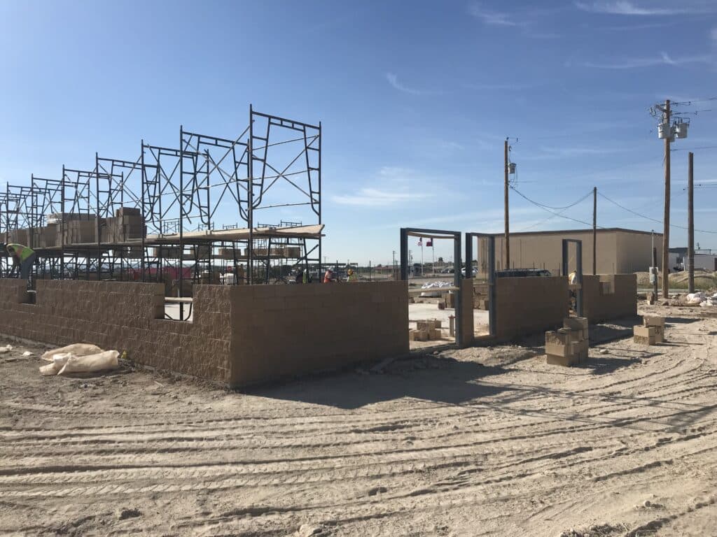 Construction site with scaffolding and partially built walls under a clear blue sky. Workers and building materials visible.