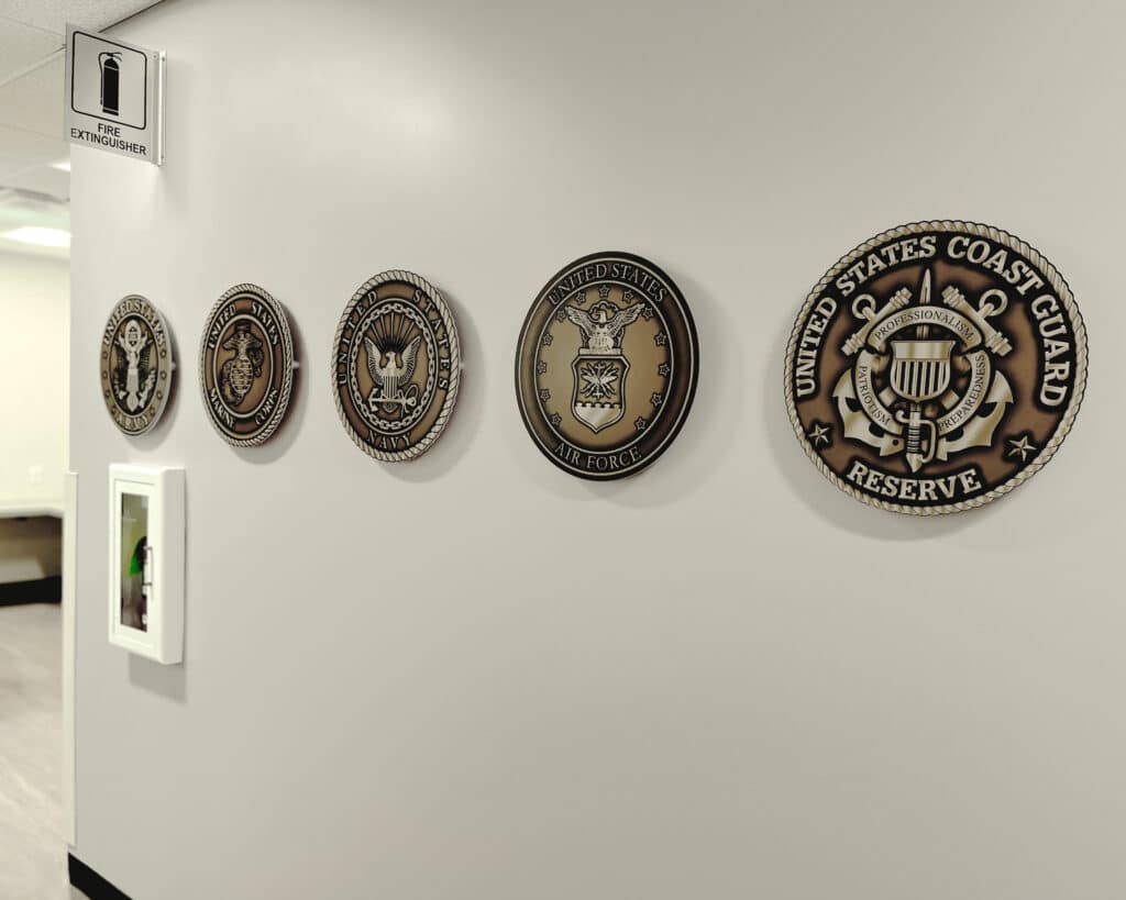 Military seals on a wall: Army, Marine Corps, Navy, Air Force, Coast Guard Reserve. Fire extinguisher sign above.