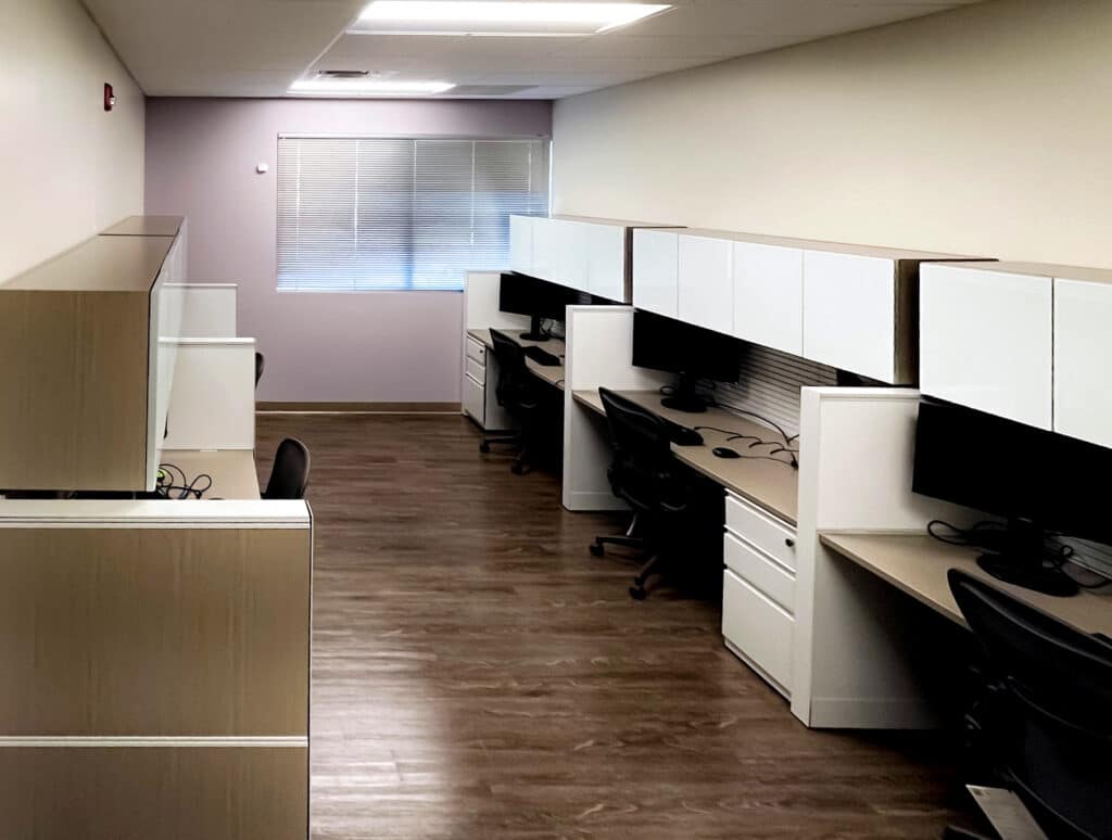 Office cubicles with desks, chairs, and overhead storage in a modern workspace.