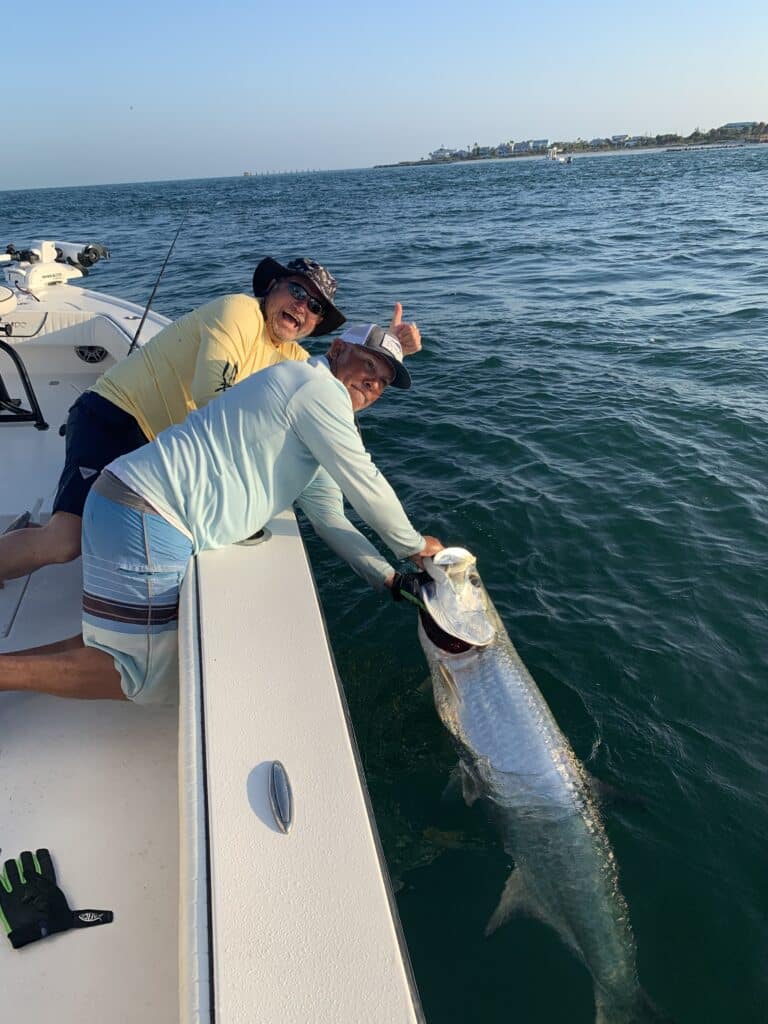 Two fishermen on a boat happily catching a large tarpon in the ocean on a sunny day.