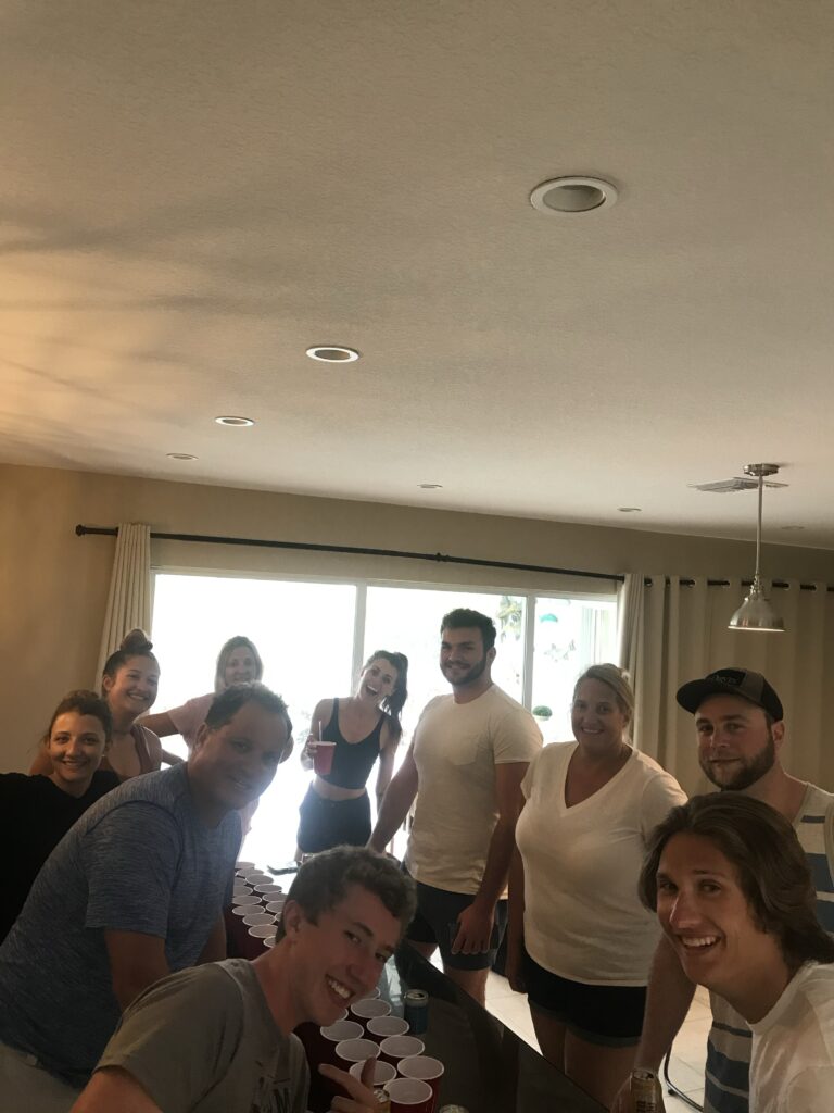 Group of friends playing beer pong indoors, smiling and holding red cups.