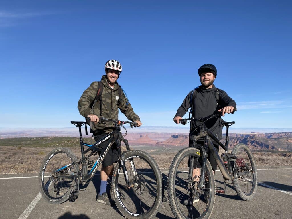 Two cyclists with mountain bikes enjoying a scenic desert landscape under a clear blue sky.